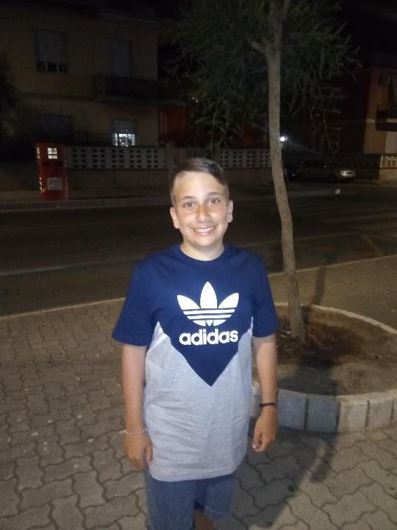 A young boy wearing an adidas t-shirt standing on a sidewalk at night with glanzmann's thrombasthenia.