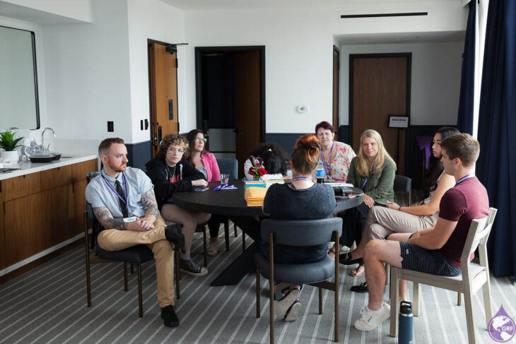 A group of people with glanzmann's thrombasthenia sitting around a table in a hotel room.
