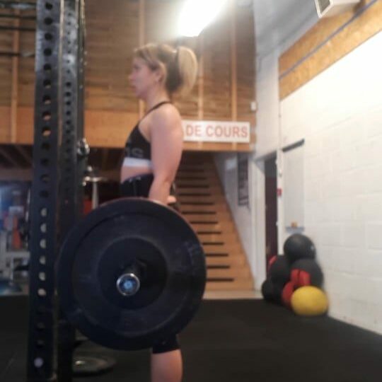 A woman standing in a gym with a barbell.