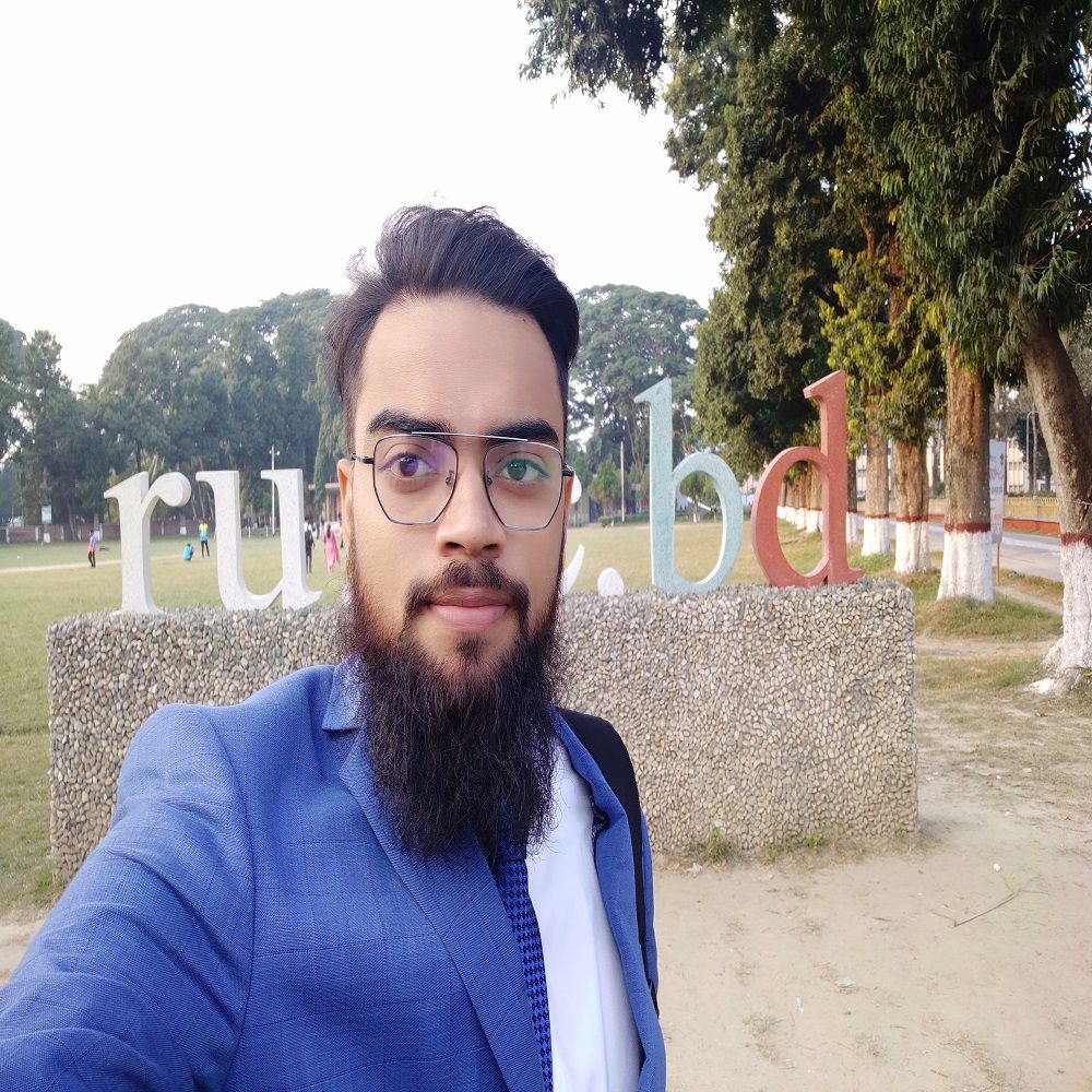 A man with a beard and glasses is taking a selfie in front of a sign.